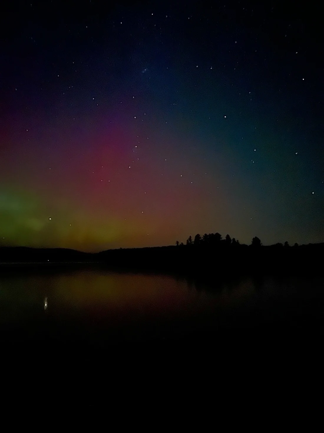 Colorful auroras and stars above a lake and silhouetted trees