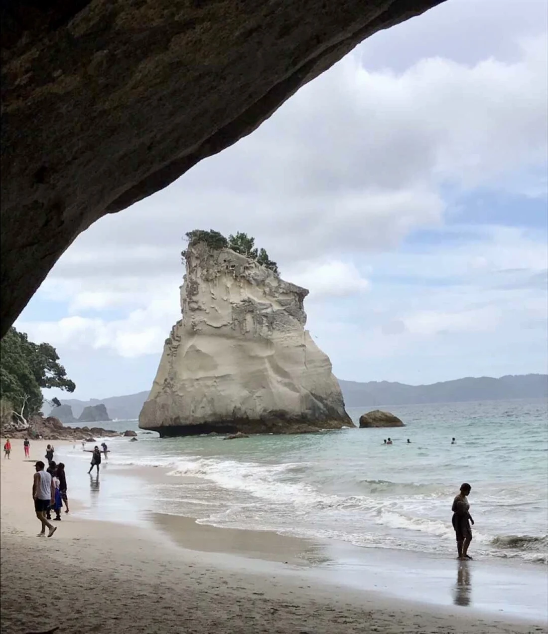 A coastal rock formation and beachgoers seen beneath a rock arch